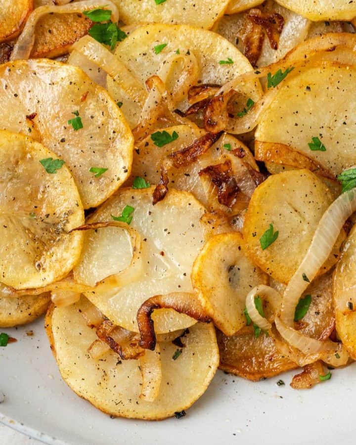 Close up of sliced browned potatoes with onions and chopped fresh parsley on top.