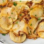 Close up of cooked potatoes Lyonnaise in a skillet with a text overlay on the photo.