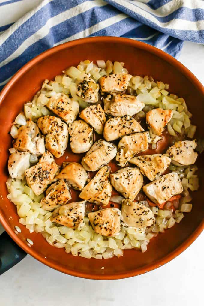 Sautéed onion and seared chunks of chicken in a copper skillet.