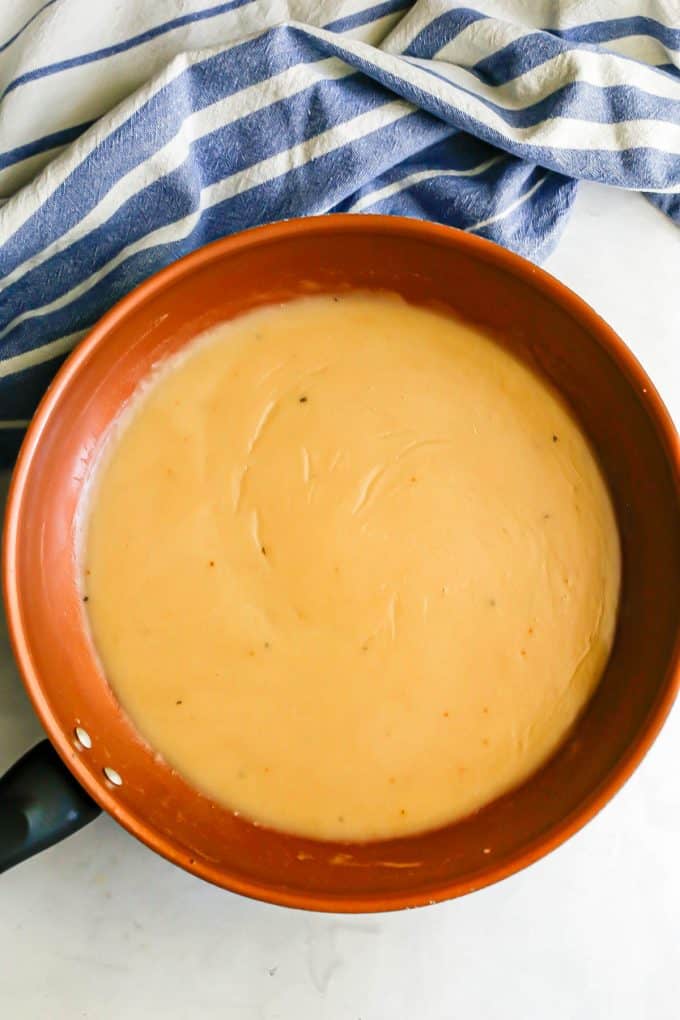 Gravy in a copper skillet beside a blue and white striped towel.