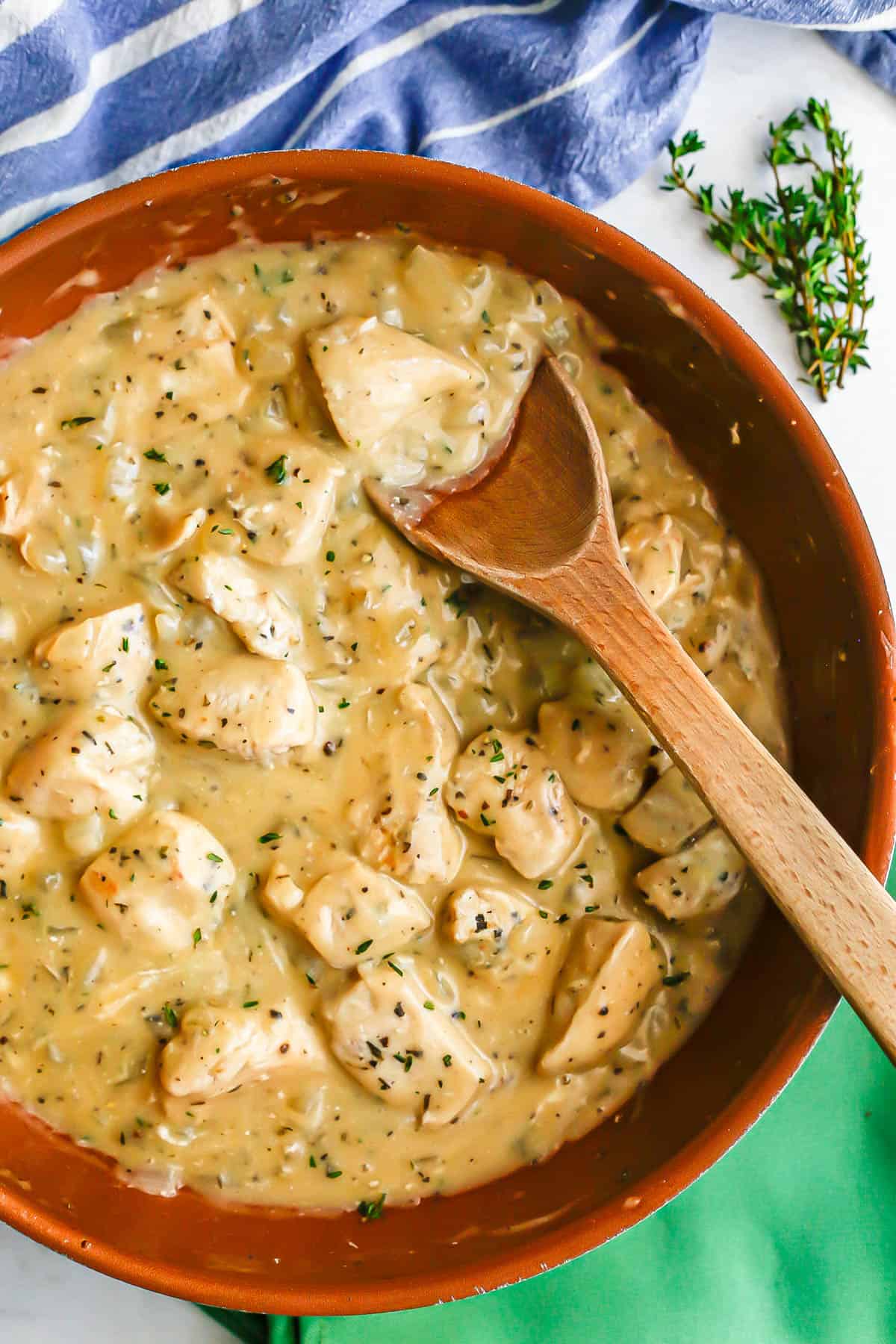 A creamy chicken and gravy mixture in a copper skillet with a wooden spoon resting in it and fresh thyme to the side.