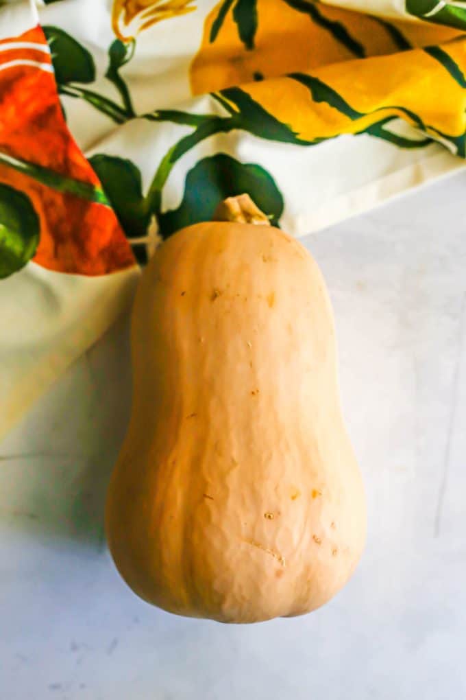 A butternut squash laid on a white counter with a colorful fall napkin to the side.