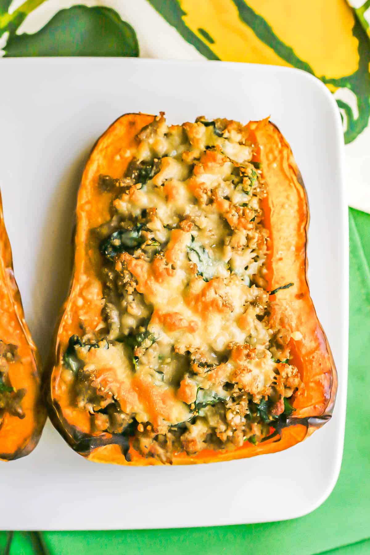 A butternut squash half with a turkey sausage and spinach mixture topped with melted, browned Parmesan cheese served on a white plate.