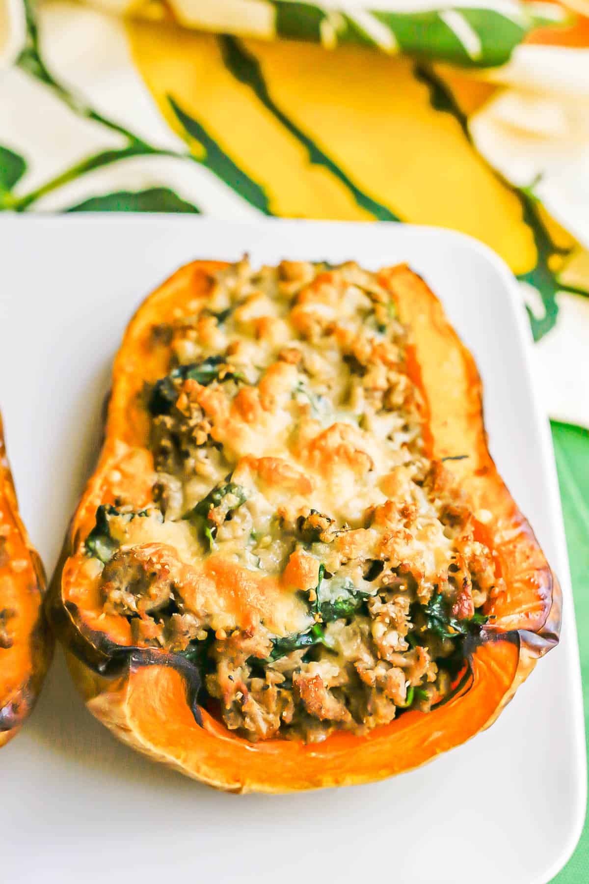 Angled view of a butternut squash half with a turkey sausage and spinach mixture topped with melted, browned Parmesan cheese.