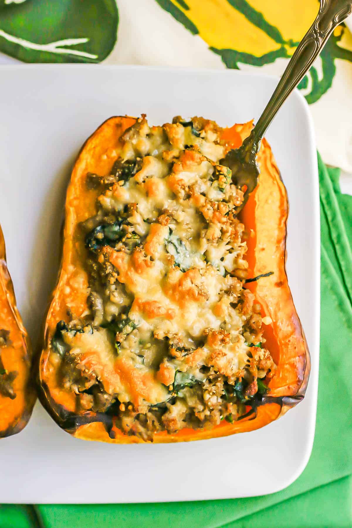 A fork sticking out of a roasted butternut squash stuffed with turkey sausage and spinach with melted Parmesan cheese on top.