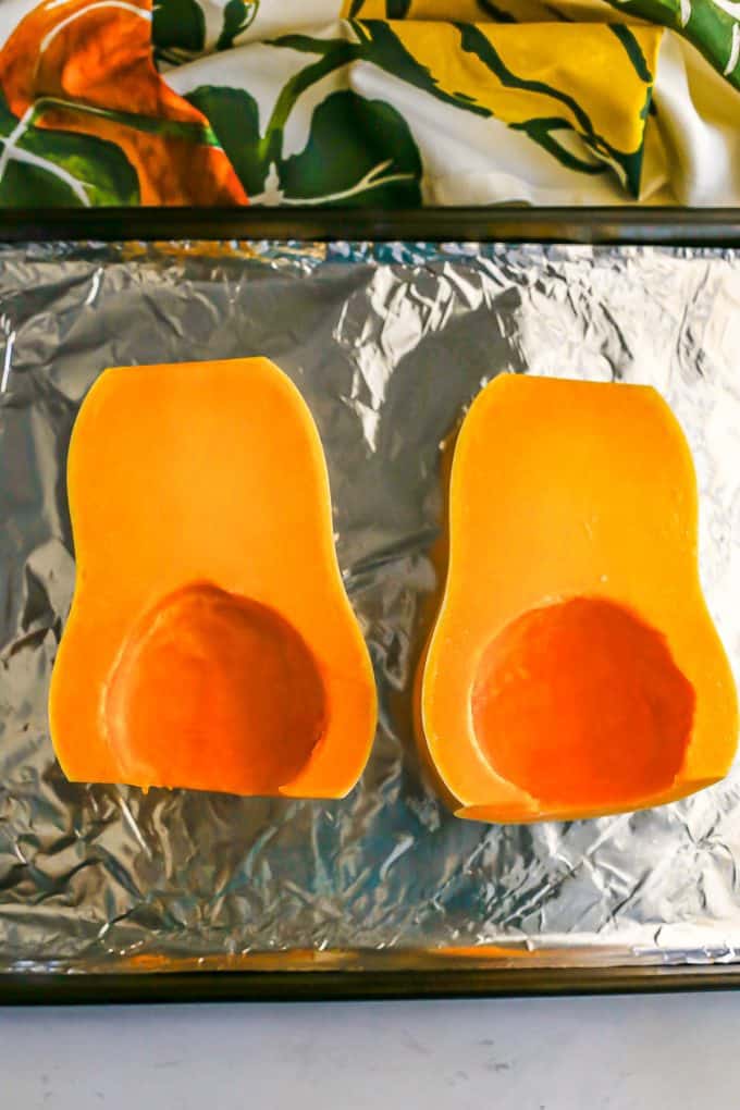 A butternut squash cut in half, with the seeds removed and placed on an aluminum foil baking pan.
