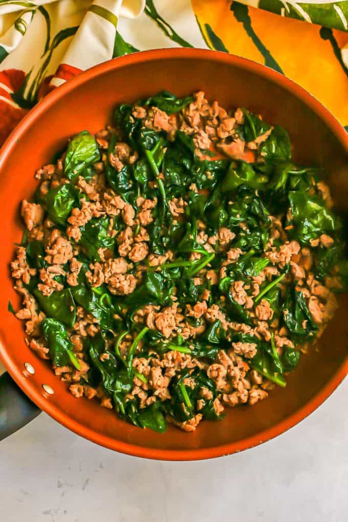 A large copper skillet with sautéed spinach and cooked, crumbled turkey sausage.