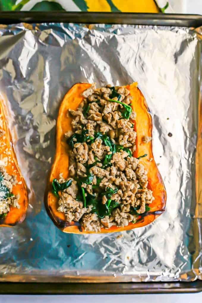 Butternut squash halves on an aluminum foil lined baking sheet filled with a turkey sausage and spinach mixture.