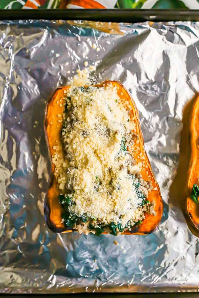 Butternut squash halves on an aluminum foil lined baking sheet filled with a turkey sausage and spinach mixture and topped with Parmesan cheeese.