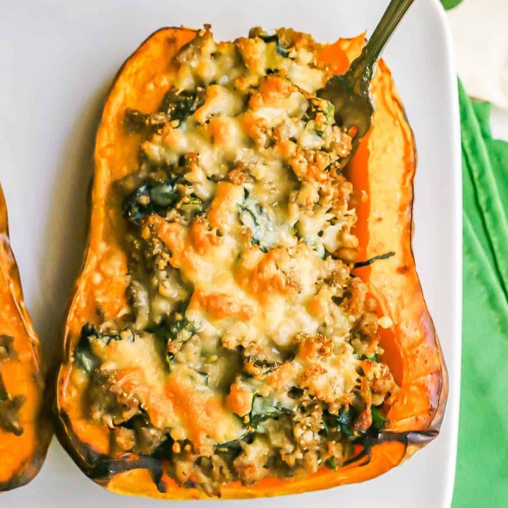 Close up of a fork sticking out of a roasted butternut squash stuffed with turkey sausage and spinach with melted Parmesan cheese on top.
