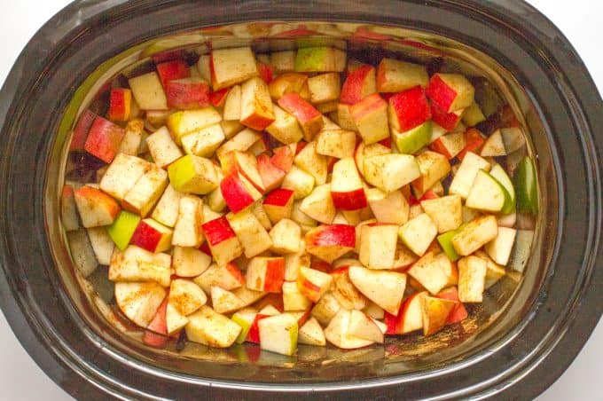 Diced red and green apples in a slow cooker with spices sprinkled on.