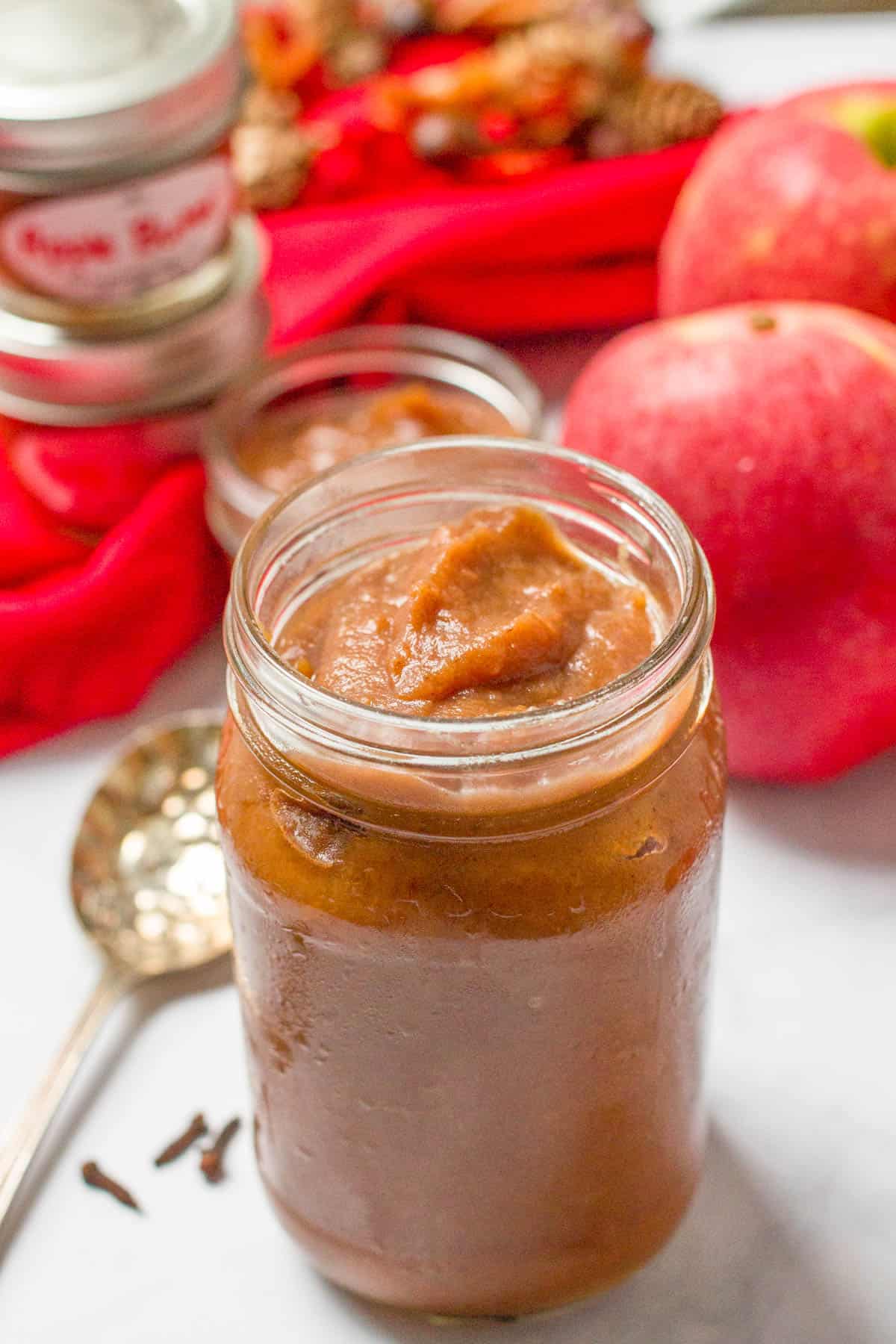 A glass jar with apple butter with apples in the background.