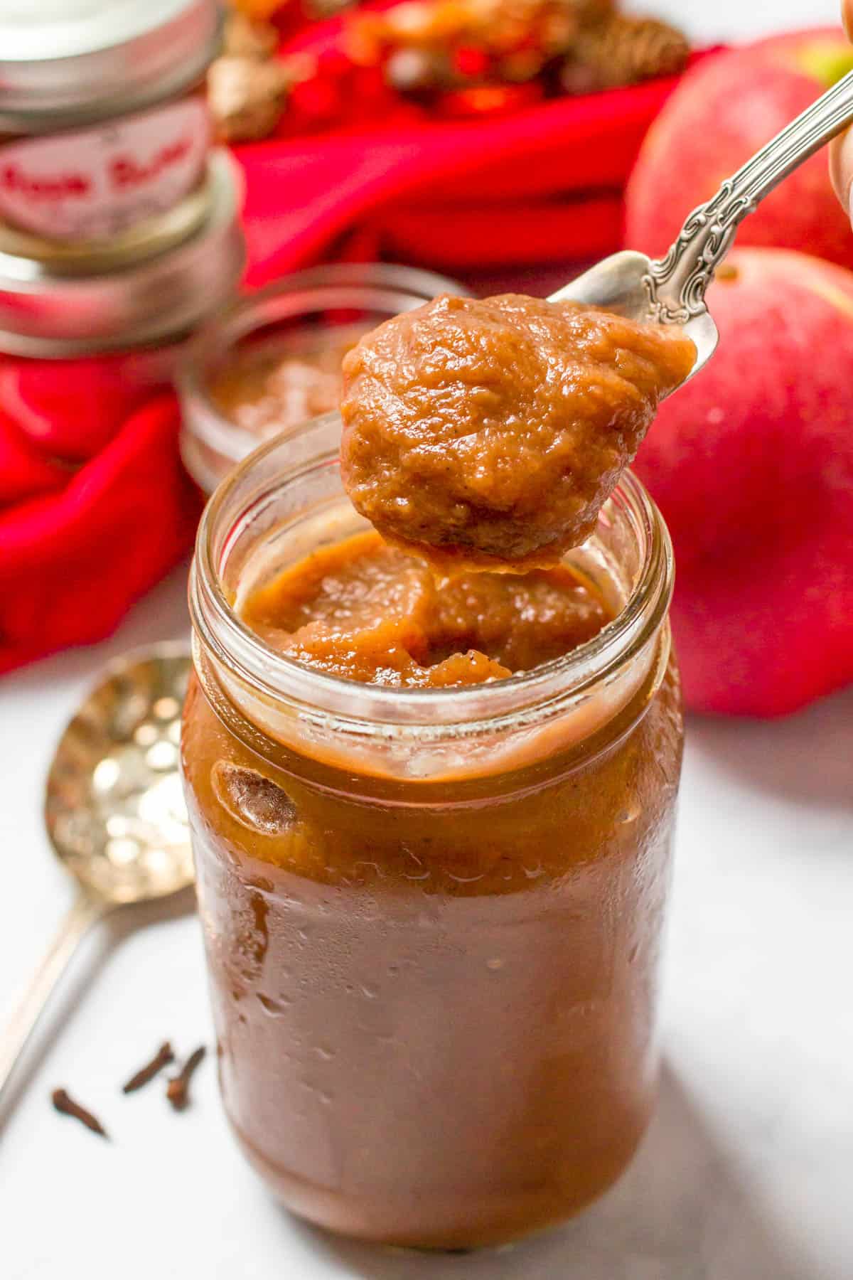 A spoon scooping up apple butter from a glass jar.