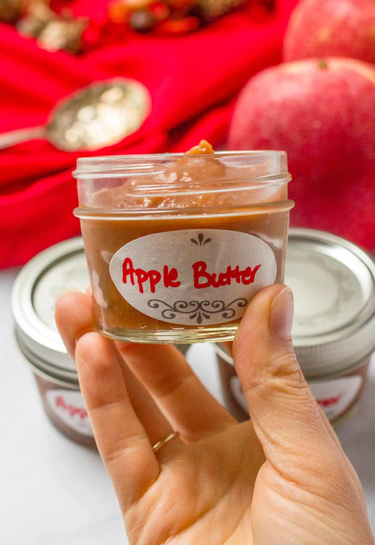 A hand holding a small glass jar with an apple butter label on it.