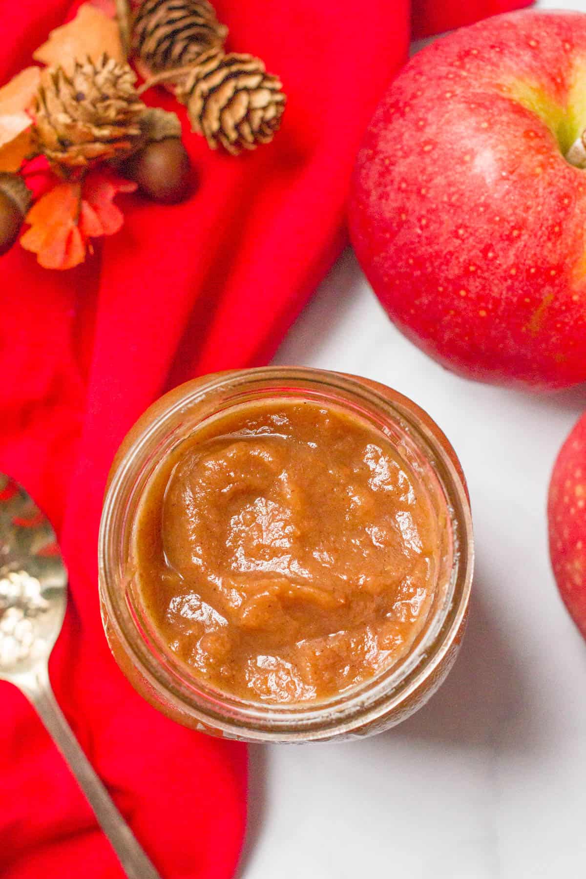 An overhead view of a jar of apple butter alongside fresh apples and a spoon.