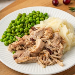Close up of slow cooker cranberry dijon chicken served with mashed potatoes and green peas.
