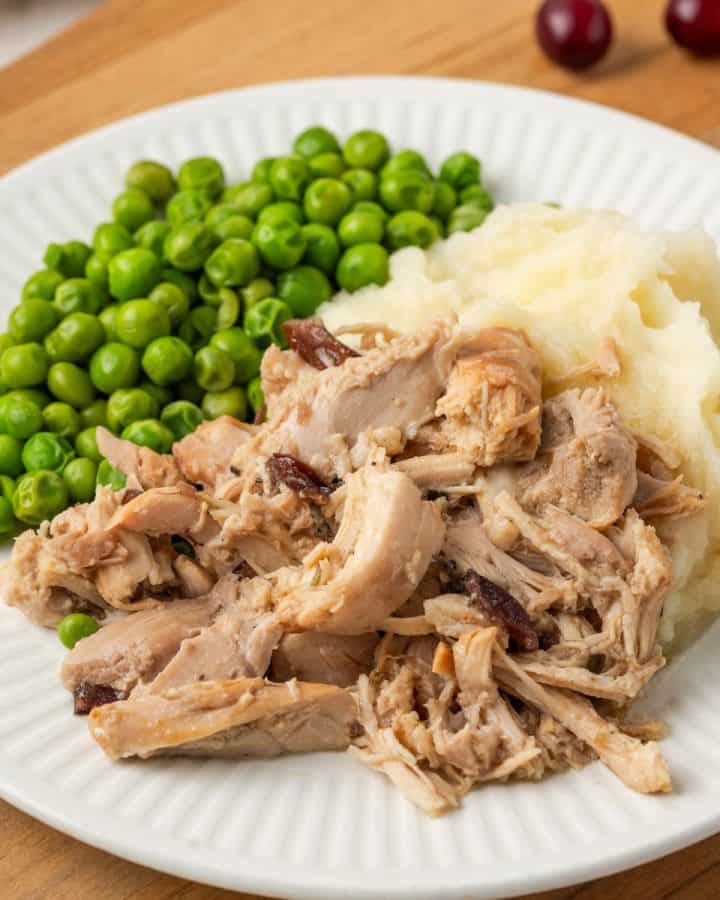 Close up of slow cooker cranberry dijon chicken served with mashed potatoes and green peas.