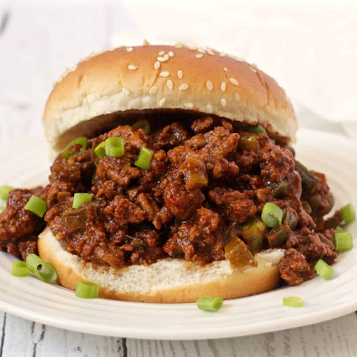 Close up of a sesame seed bun filled with a ground turkey sloppy Joe mix sliced green onions sprinkled all over.