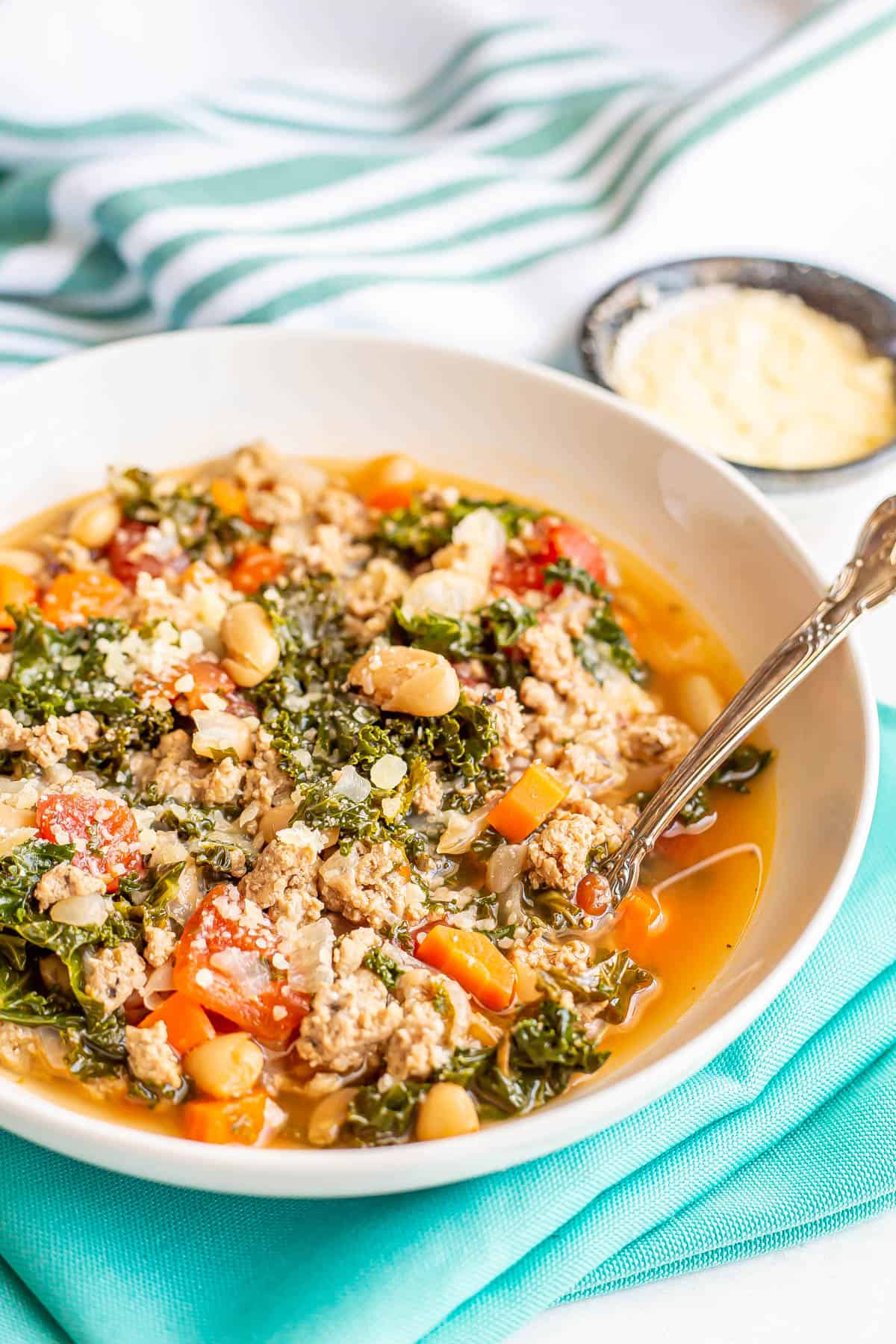 A spoon tucked into a bowl of ground turkey soup with kale and white beans.