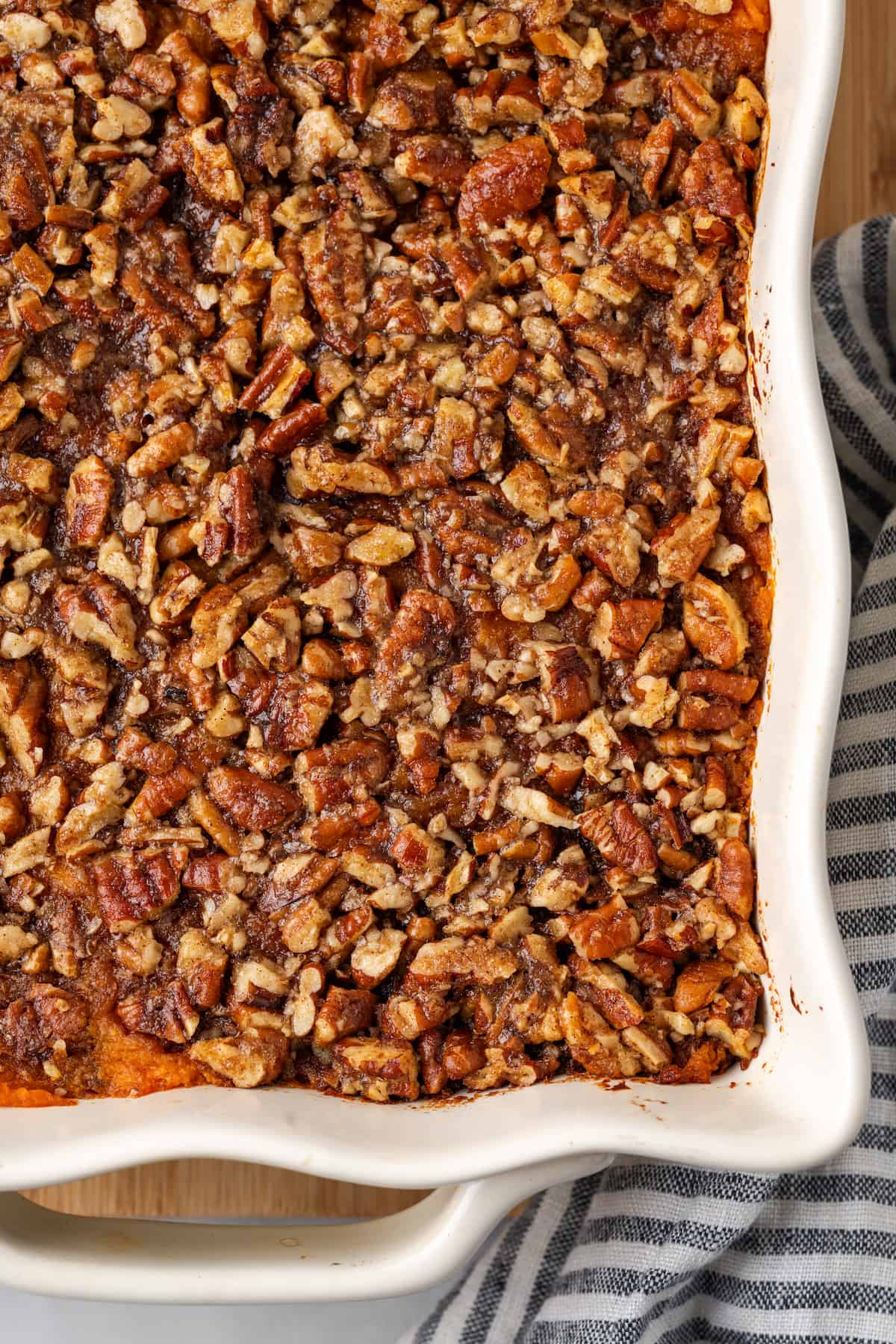Baked bourbon sweet potato casserole with a pecan topping in a fluted white casserole dish.