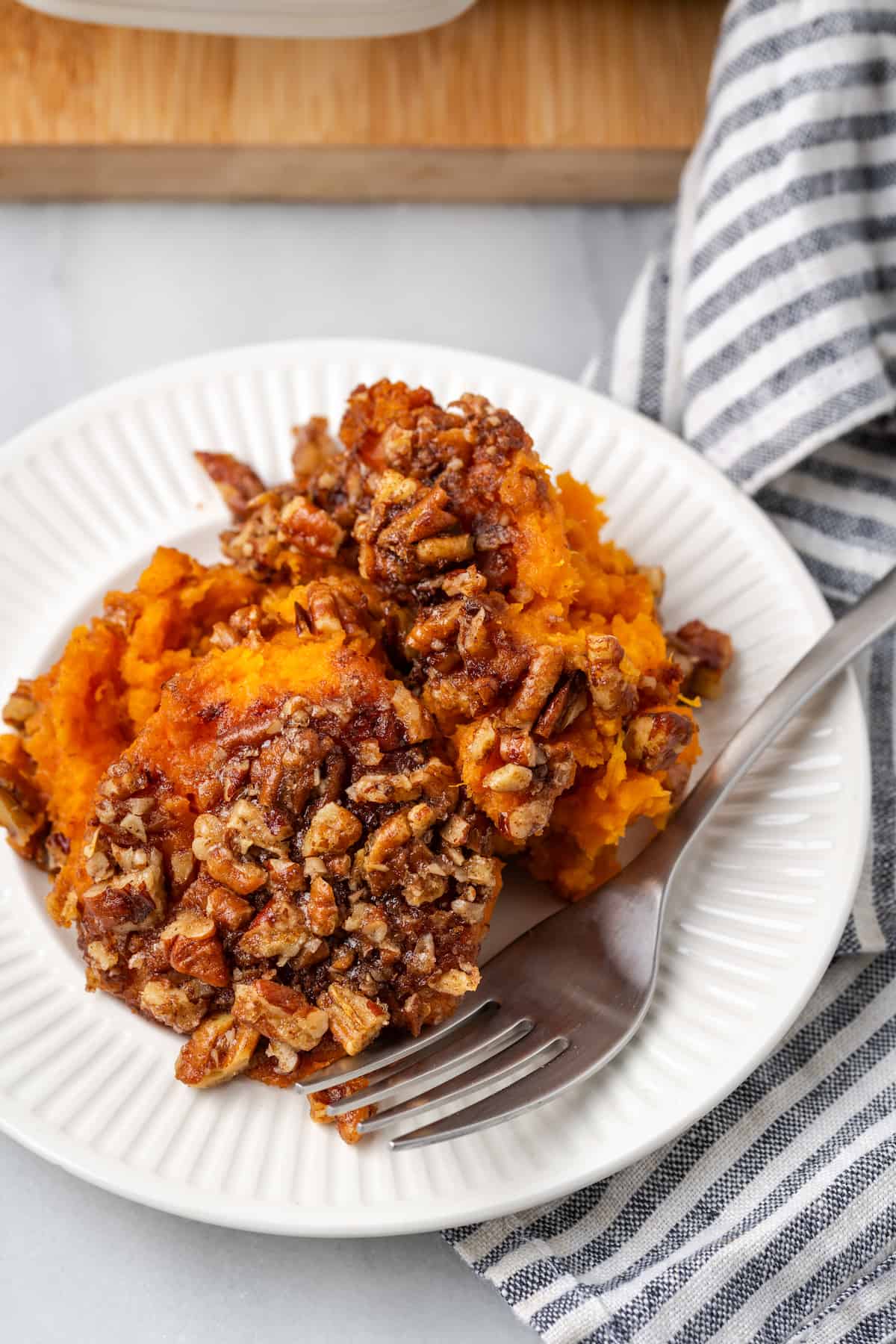 Bourbon sweet potato casserole with a pecan topping served on a white plate with a fork.