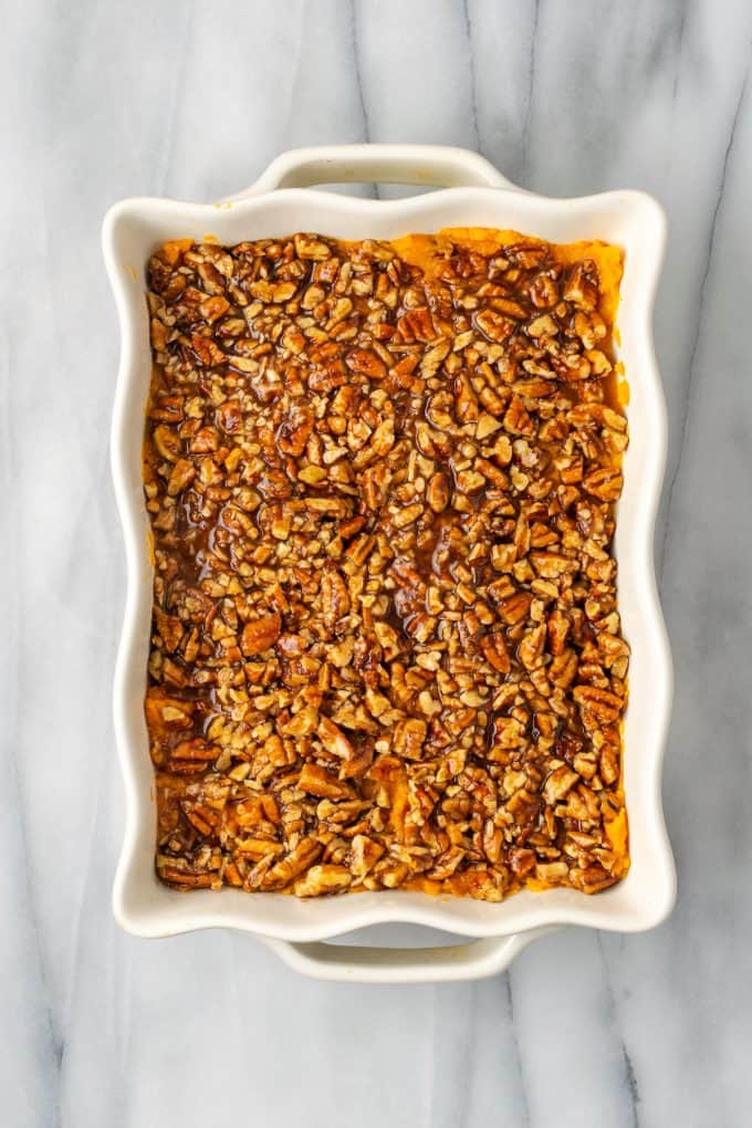 A white casserole dish with mashed sweet potatoes topped with a buttery pecan streusel.