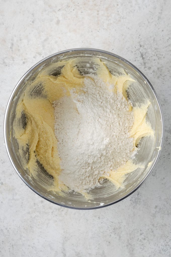 A metal mixing bowl with creamed butter and sugar and a flour mixture added on top.