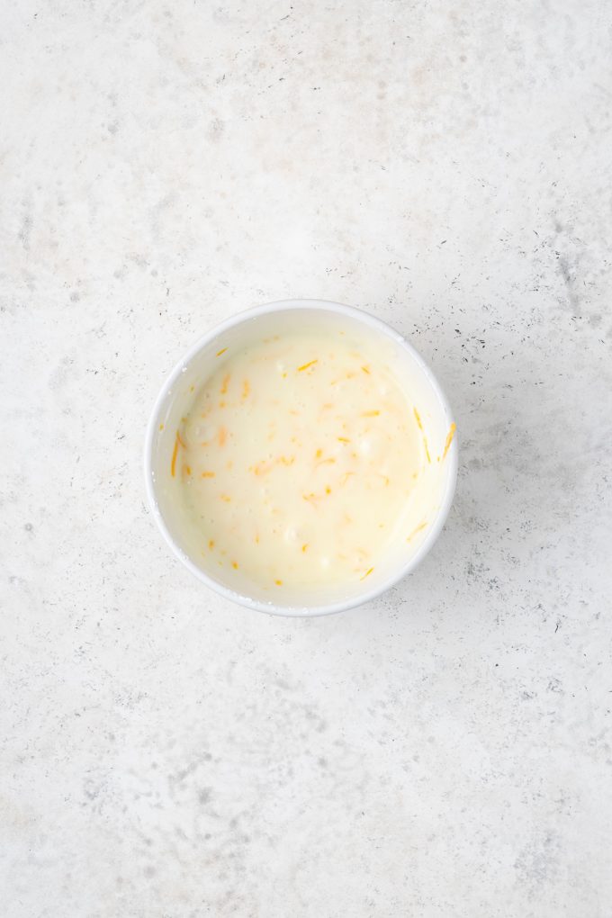 A small white bowl of a cake glaze with orange zest in it.
