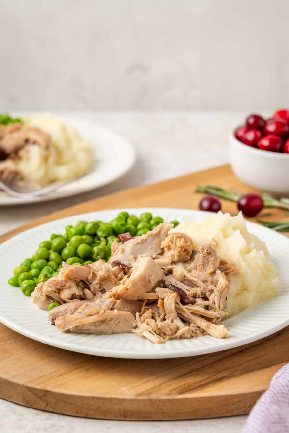Shredded crock pot cranberry Dijon chicken served alongside mashed potatoes and peas on a white dinner plate.