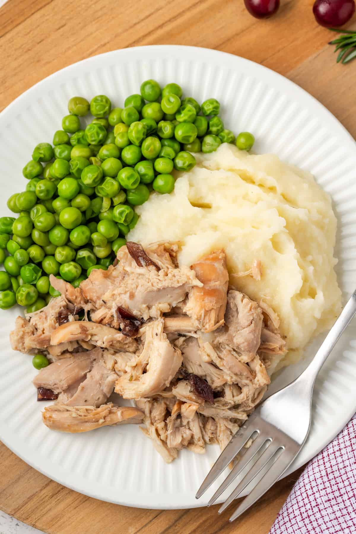 Cranberry Dijon chicken served alongside mashed potatoes and peas on a white dinner plate with a fork resting to the side.
