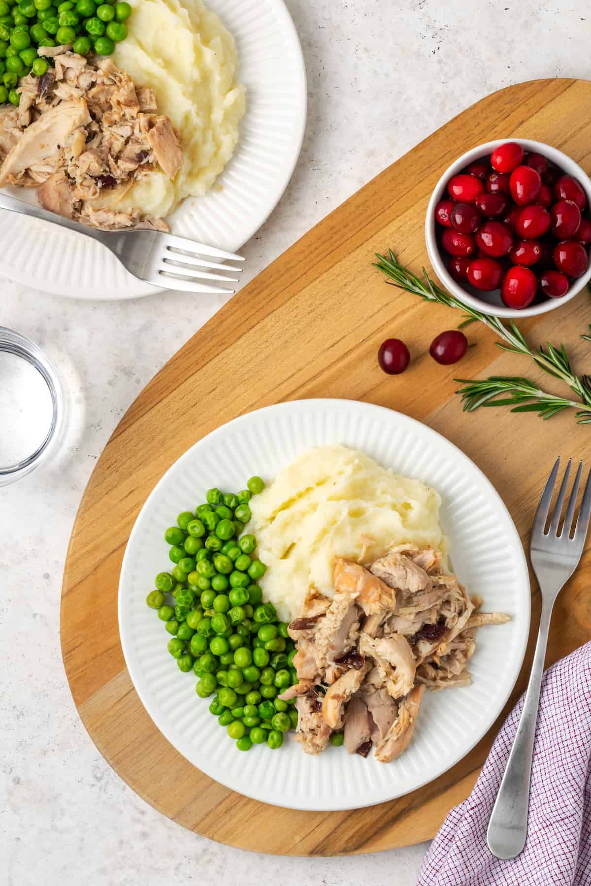 Two dinner plates with cranberry dijon chicken alongside mashed potatoes and green peas.