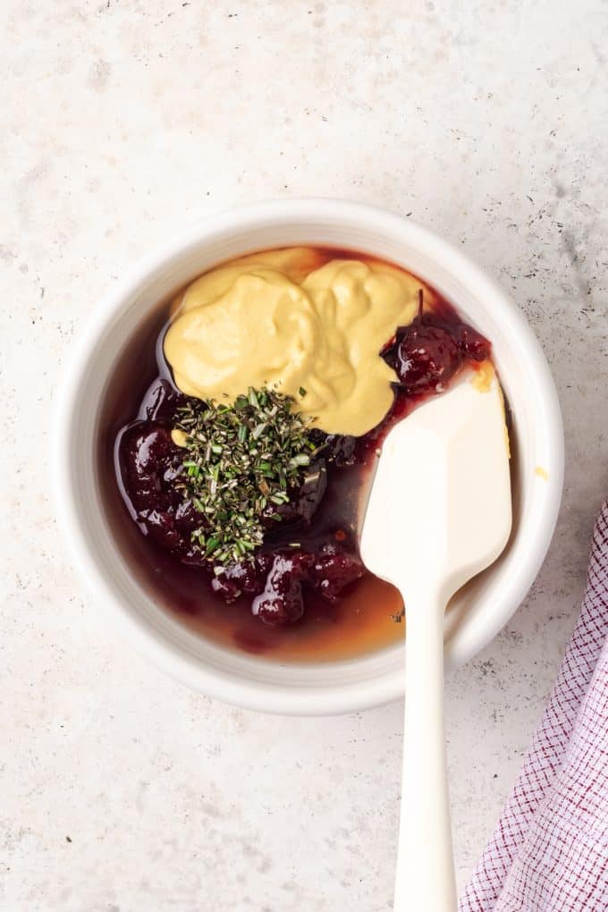 A small white bowl with cranberry sauce, Dijon mustard and seasonings before being mixed together.