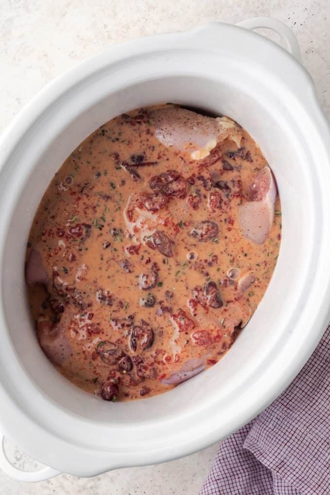 Chicken in a crock pot with a cranberry Dijon sauce before being cooked.