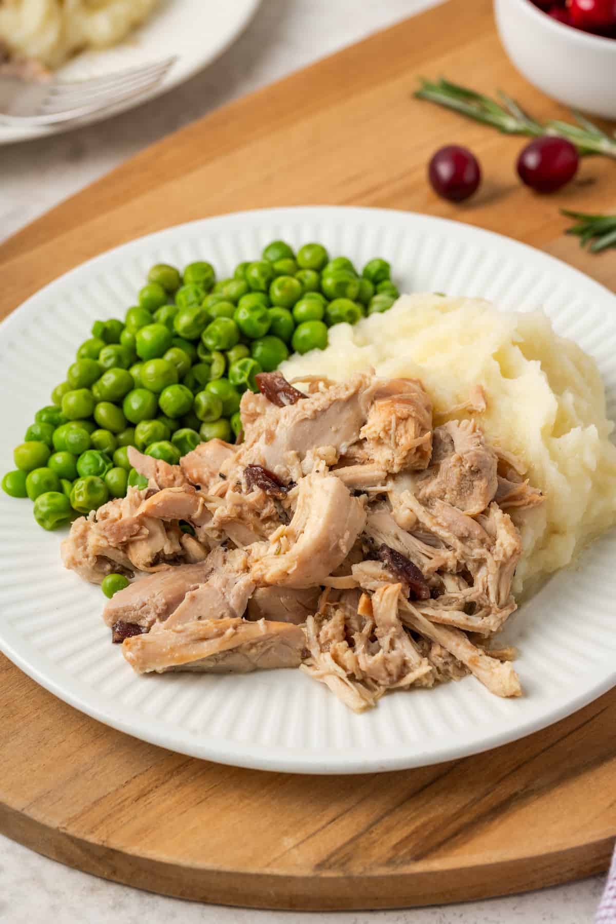 Cranberry Dijon chicken served alongside mashed potatoes and peas on a white dinner plate.