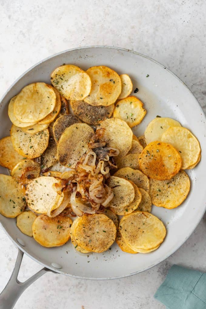 Sliced browned potatoes along with cooked onions and seasonings in a skillet.