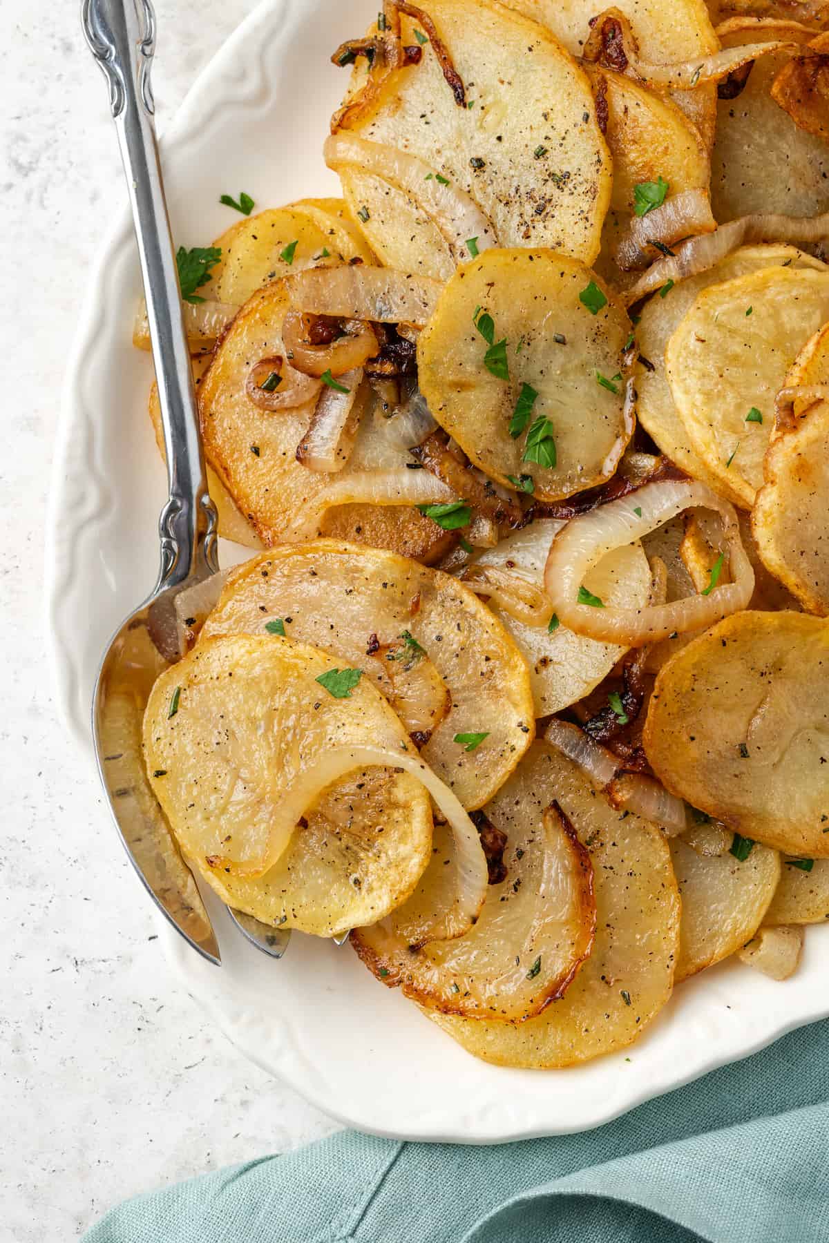 Potatoes Lyonnaise served in a white serving dish with a serving fork tucked in.