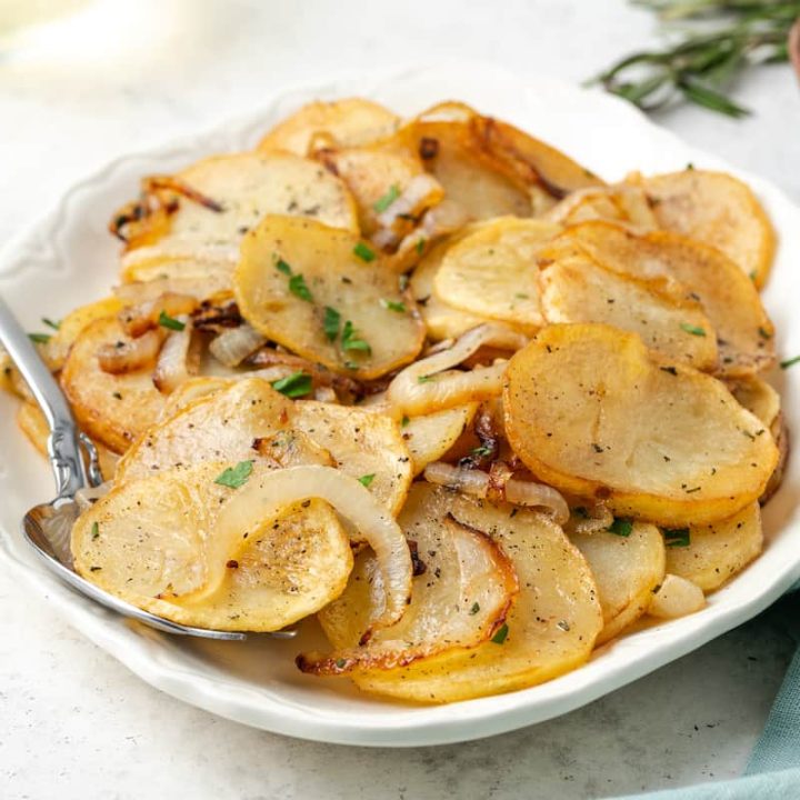 A serving dish with potatoes Lyonnaise with a serving spoon tucked in.