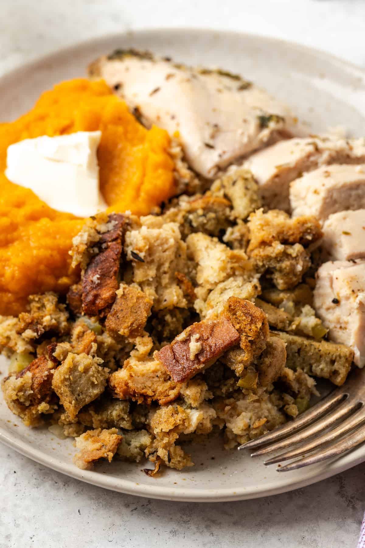 A dinner plate with Thanksgiving dressing, sliced turkey and sweet potato casserole.