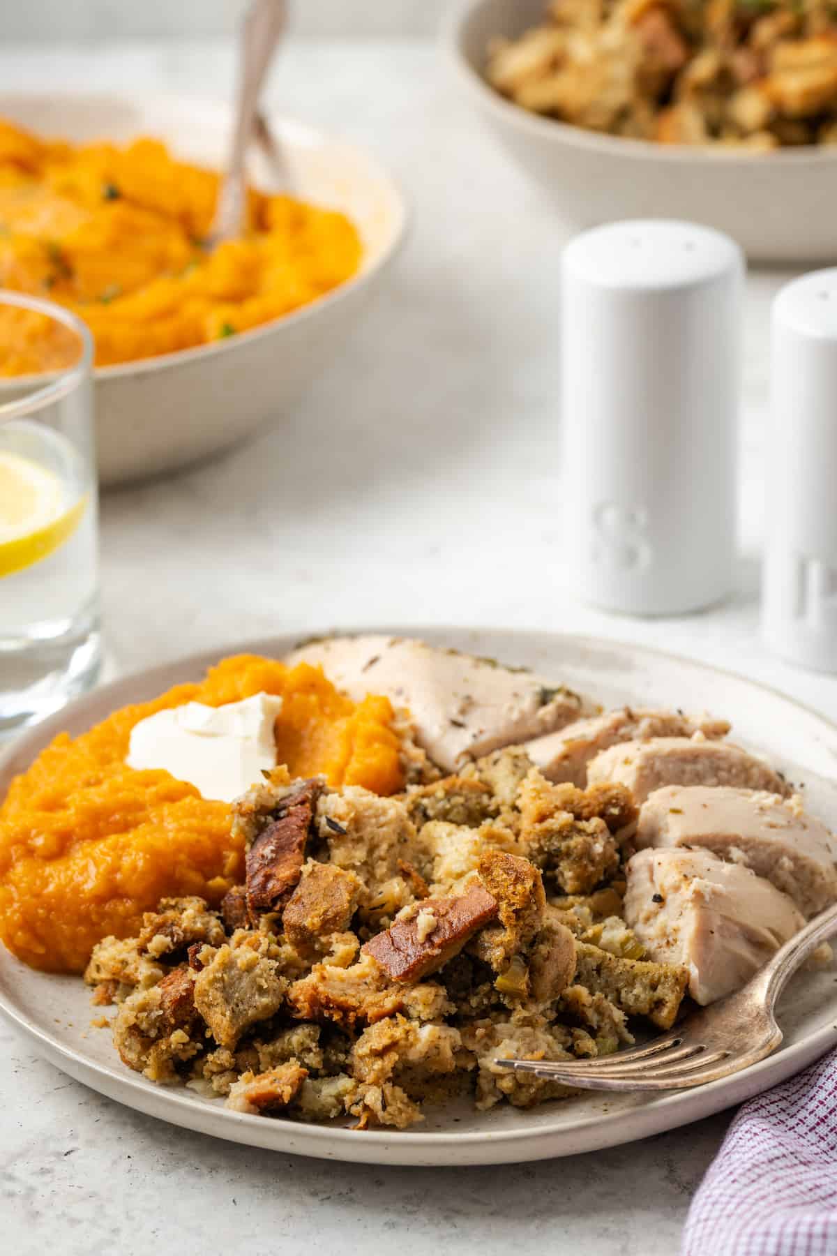 A dinner plate with sliced turkey, sweet potatoes and holiday dressing with a fork resting to the side.