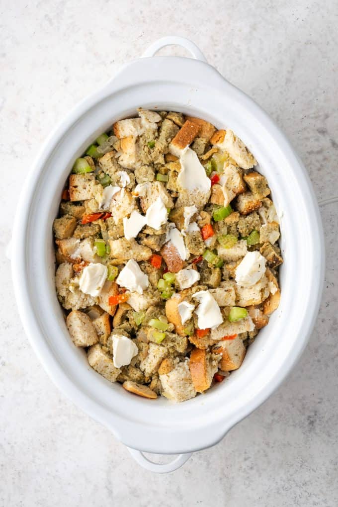 A white slow cooker with a mix of bread and veggies and butter dotted on top.