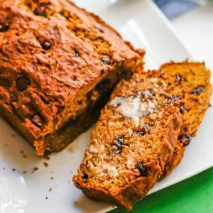 Slices of chocolate chip zucchini bread cut off from the loaf and resting on a white platter.