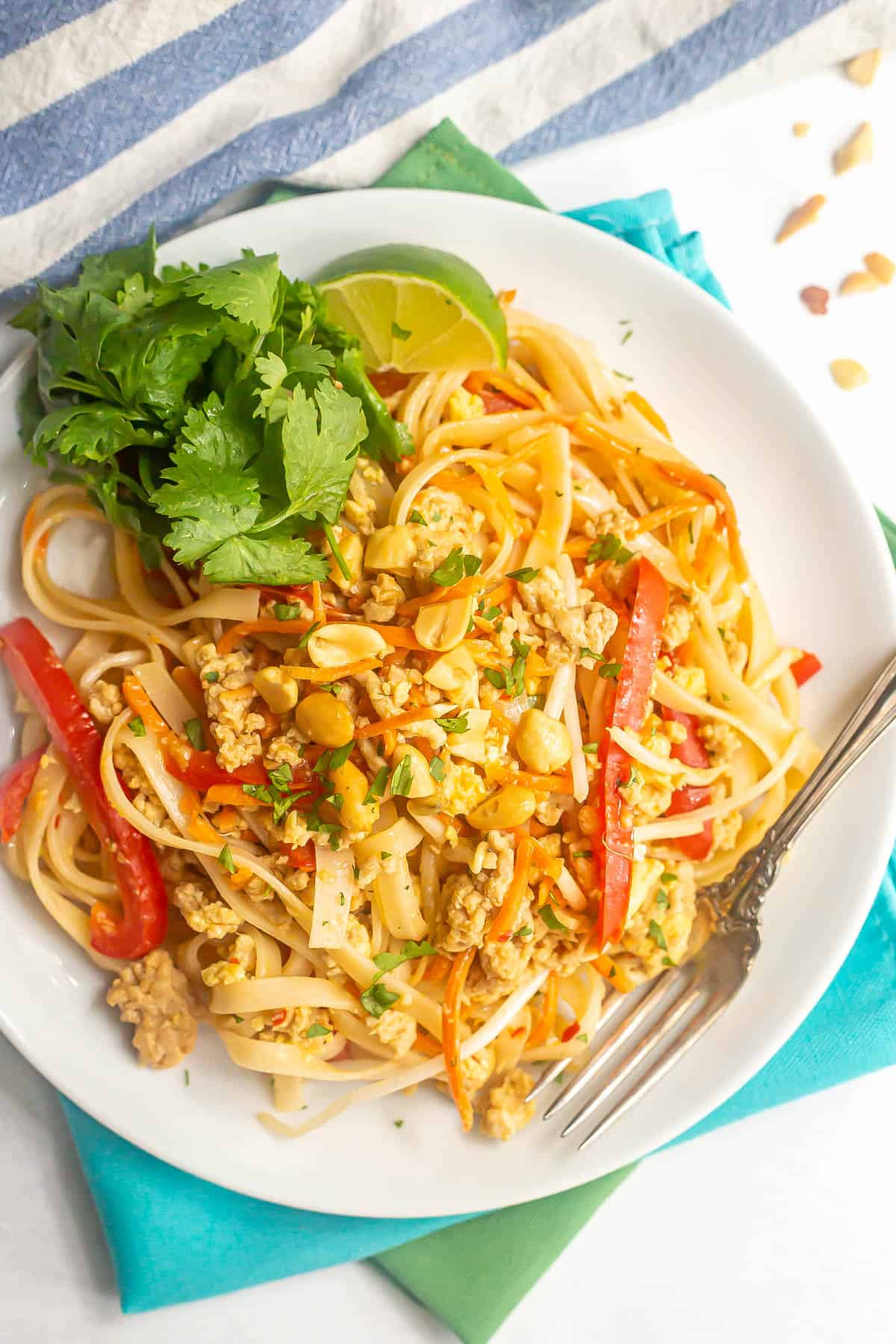 Easy chicken pad Thai served on a white plate with peanuts, cilantro and lime wedges and a fork to the side.