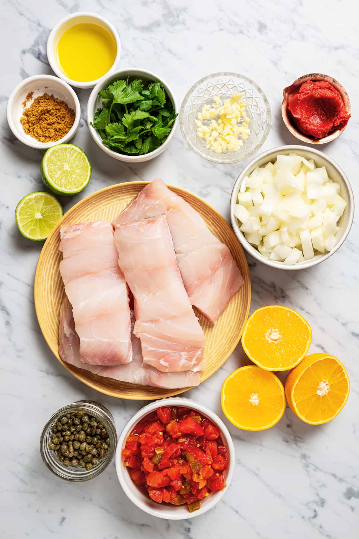 Ingredients laid out for a grouper recipe with onion, tomatoes and lemon.