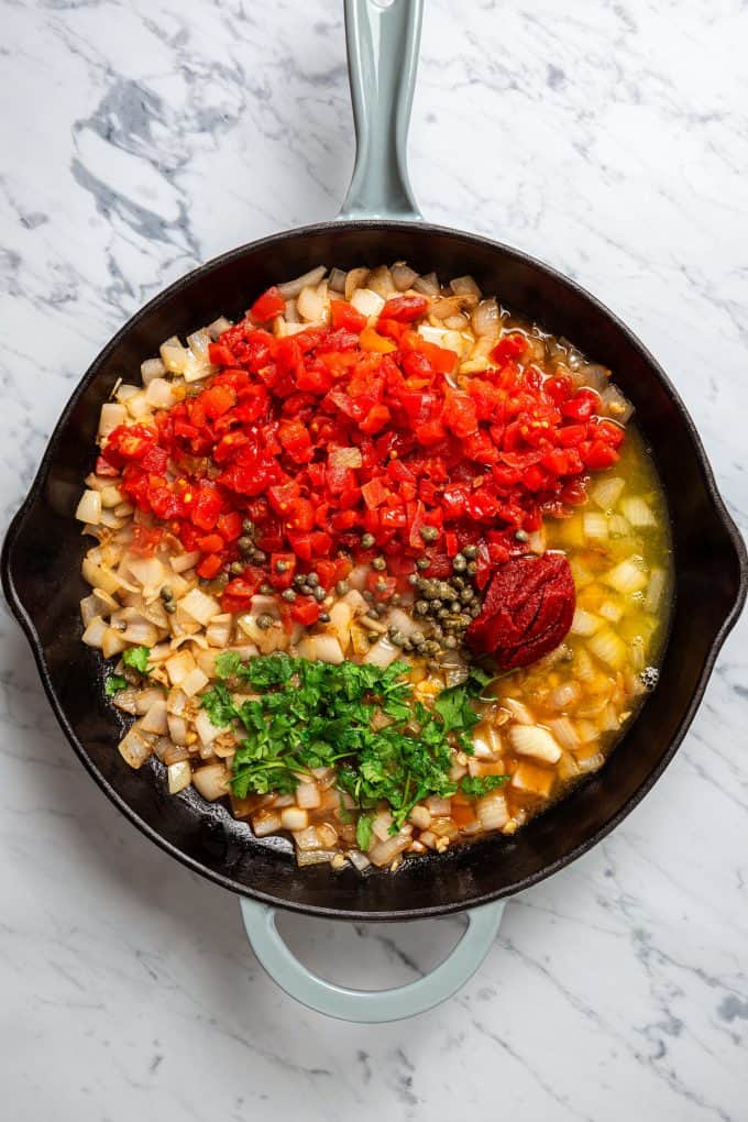 Sautéed onions topped with tomatoes, tomato paste, capers, seasonings and herbs before being stirred together in a skillet.