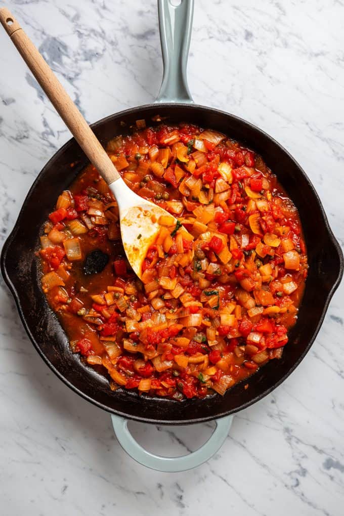 A tomato based sauce being stirred together in a large skillet.