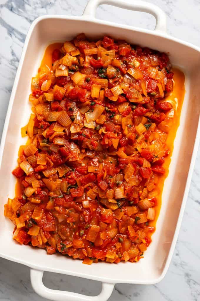 Grouper filets covered with a tomato based sauce in a large casserole dish before being baked.