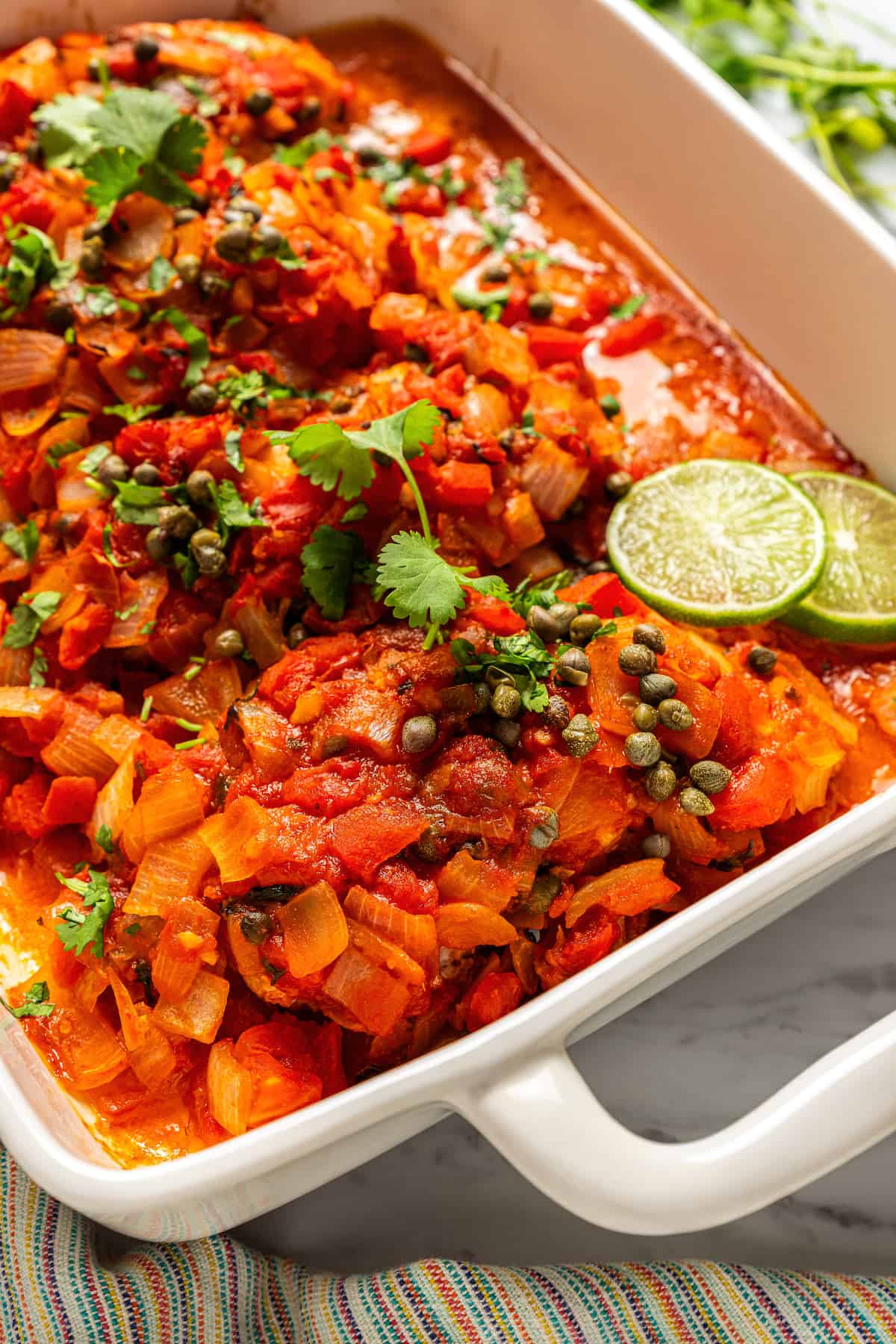 Close up of a grouper filet in a tomato based veracruz sauce in a white casserole dish.