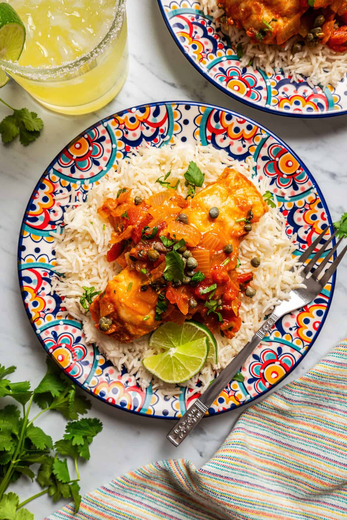 Baked grouper veracruz served over rice with extra sauce on a colorful plate with a fork to the side.