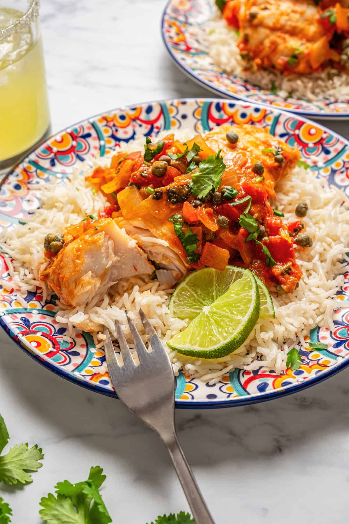 A fork resting on a plate with a grouper filet topped with a tomato and caper sauce.