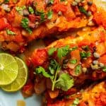 Close up of grouper veracruz served on an oval platter with fresh herbs and lime slices and a text overlay on the photo.
